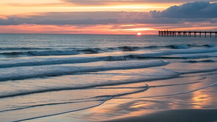 Sunset over the ocean with gentle waves and a distant pier on the beach