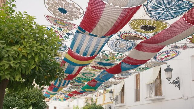 Crocheted flags and doilies represent countries worldwide, forming a vibrant canopy over a charming street in Spain.