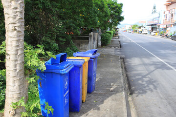Three blue trash cans are lined up on the sidewalk