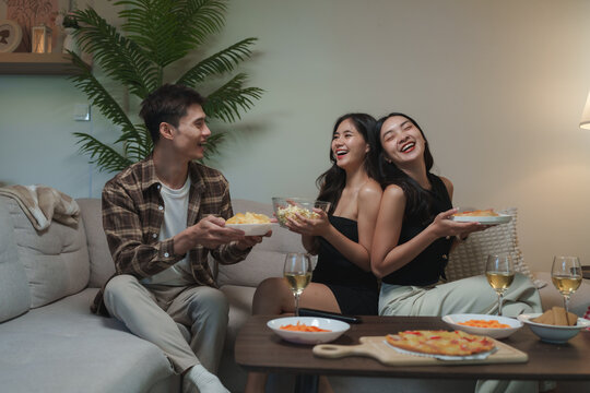 Young friends sharing snacks, laughing at home party - Powered by Adobe