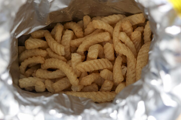 Satisfying close up view looking inside an open foil bag filled with crunchy yellow snack. This delicious, ridged junk food offers salty treat for munching