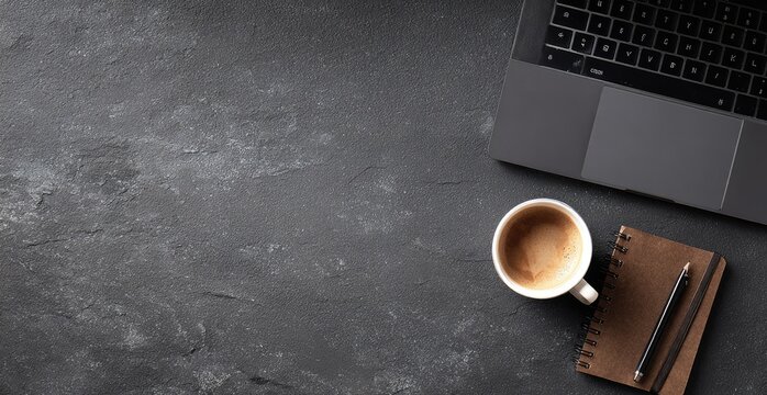 Flat lay of laptop, coffee, notebook, and pencil arranged on a textured, dark-colored surface