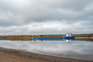 A barge floats along the river against the backdrop of an autumn forest.