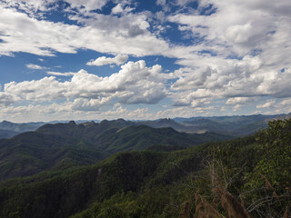 Expansive panoramic vista of verdant mountain ranges, possibly Northern Thailand's Mae Hong Son province, stretching into the horizon under a dramatic sky with scattered cumulus clouds. Captures