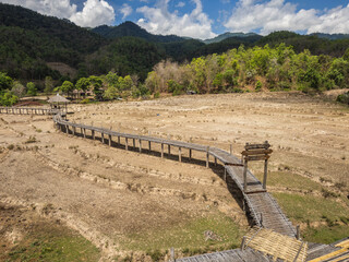 A winding wooden bamboo walkway stretches across arid terraced fields towards distant green...