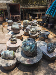 Collection of unique handcrafted ceramic pottery with metallic glazes displayed outdoors at a traditional artisan workshop in Northern Thailand. Evokes a sense of rustic artistry.