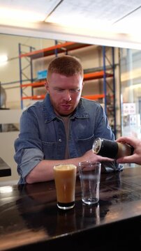 Redhead man sitting at a craft brewery bar smiling while a bartender pours him a glass of nitro cold brew coffee from a can in slow motion