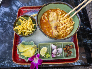 Authentic Khao Soi, a Northern Thai curry noodle soup with tender chicken and egg noodles, served with crispy fried noodles, pickled greens, fresh lime, red onion, scallions, and chili flakes. A