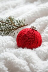 Red knitted Christmas ball and pine branch on soft white blanket creating cozy winter festive composition