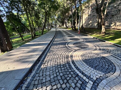 Cobbled stone walkway with artistic circular pattern design in a shaded park surrounded by green trees and sunlight. Scenic urban pathway with natural light and historical atmosphere.