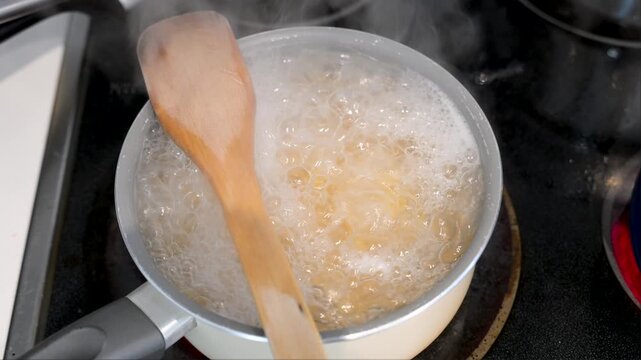 The simple comfort of a home-cooked meal is captured in this shot of pasta boiling in a saucepan. A wooden spoon on the pot adds to the authentic, rustic feeling.