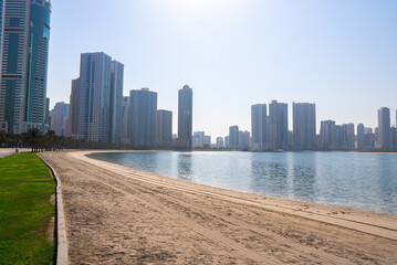 Clean beach with turquoise sea and tall skyscrapers in the distance under clear sky. 