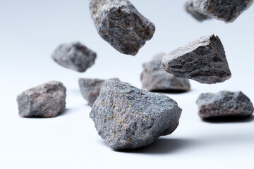 Gray volcanic rocks captured in mid-air and resting on a white surface, showcasing their rough texture and irregular shapes against a clean, minimalistic background