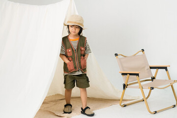 Little boy wearing explorer outfit and bucket hat walking out of indoor tent setup, showing curiosity, independence, and imaginative play in a cozy minimalist environment.