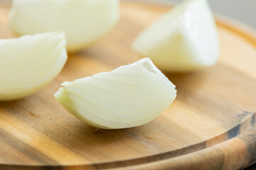 yellow onion cut into quarters on wooden round cutting board close up