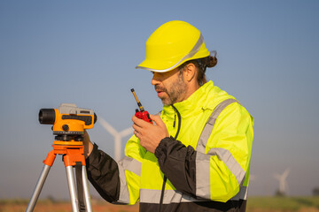 Engineer working in front of wind turbines for checking wind turbines of the field during beautiful sunset. Alternative energy concept.