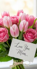 Close-up bouquet of pink tulips and roses with handwritten “Love You Mom” greeting card, bright background