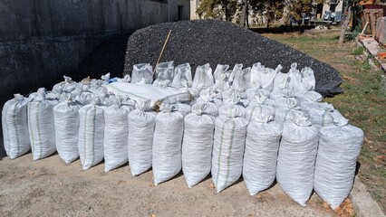 A large pile of black coal for heating and a lot of white bags filled with coal