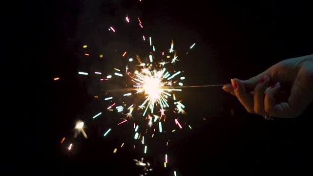 Woman hand holding a burning sparkler. Diwali, Christmas and new year sparkler background. Celebrating holidays and festival with fireworks. Burning sparkler on black background.
