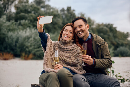Happy couple taking selfie while drinking champagne during autumn picnic day. - Powered by Adobe