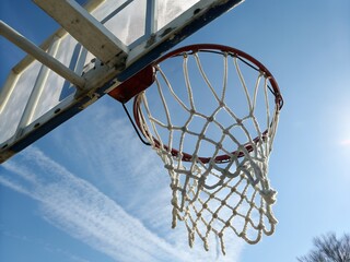 A low angle view of a basketball hoop and net against a blue sky with wispy white clouds overhead