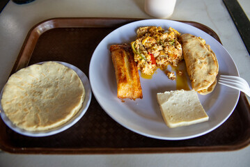 This is a top down studio shot of a fresh food meal consisting of eggs, tamal, cheese and stuffed tortilla on a plate.