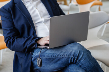 Senior business professional wearing a jacket and jeans using a sleek laptop at a modern corporate event. High quality photo