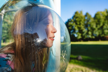 Girl playing outdoors in bubble at playground on sunny summer day