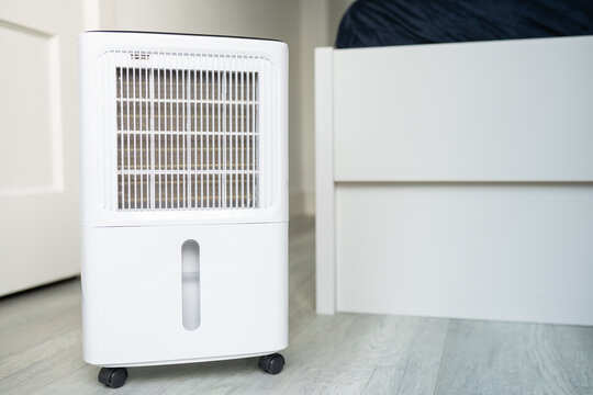 Modern white air dehumidifier positioned beside a bed in a cozy bedroom, enhancing indoor air quality and comfort in a stylish living space