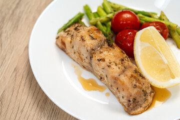 Red snapper steak, asparagus, tomatoes, and lemon on a white  plate on wooden background. Table top view.