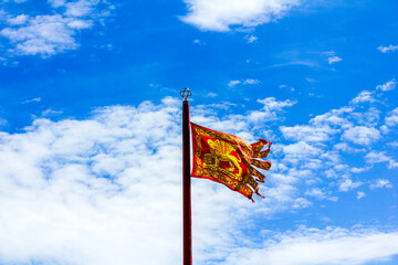 The iconic red and gold flag of Saint Mark with the winged lion, the symbol of the Republic of Venice, set against a bright blue sky. 