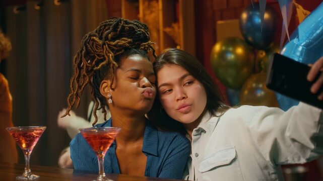 Young adult woman taking selfies with her African American friends when two men inviting them to dance, celebrating birthday in bar