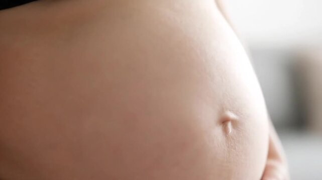 Close Up of Pregnant Woman's Stomach with Navel on a Soft Focus White Background in Natural Lighting