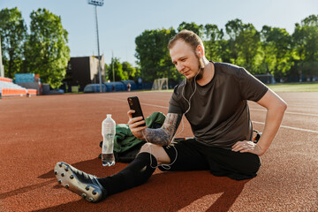 A man looks at the phone and listens in earphones while sitting on a running track