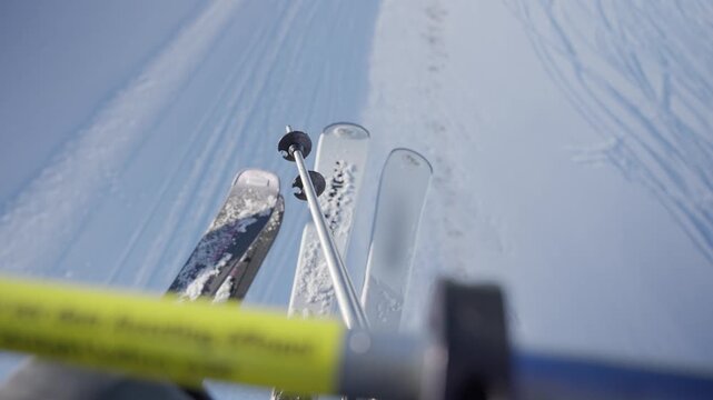 POV skiers going up on chair life in ski resort with their skies resting on bar. Transport from slope to slope during winter season vacation. Looking downhill as lift goes up mountain during daytime
