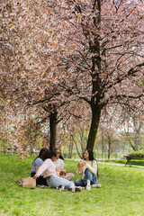 A group of four female students eat and sit on a blanket while one of them puts down a package