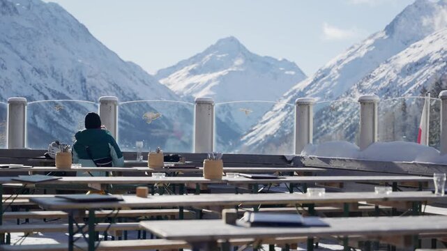 Woman skier or snowboarder enjoys rest from the slopes in restaurant on mountain. Female tourist or athlete doing extreme sport having peaceful lunch break in cafe or bistro with view to European Alps