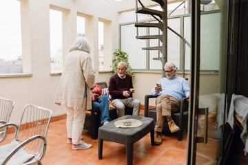 Fototapeta premium A group of three friends sit on chairs and hold phones while one of them looks at a female friend standing next to them