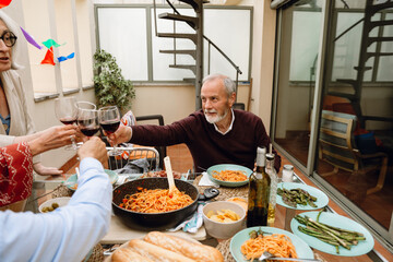 A man sits at a table and clinks glasses with a group of three friends next to him