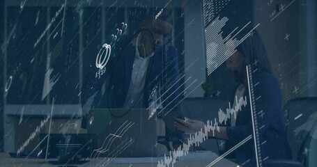 Leaning businessman collaborating with seated businesswoman at office desk, with laptop smartphone