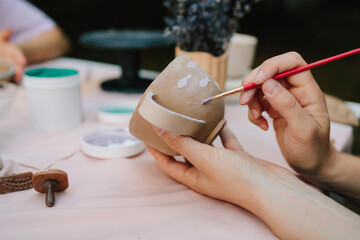 Painting ceramic mug with purple fish using brush and paint. Ceramic painting of mug with fish pattern using brush strokes. Artist paints delicate purple fish on a handmade clay mug.