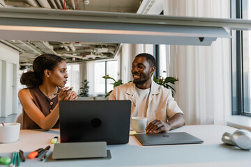A male worker smiles while sitting at a table next to a female worker who is talking