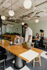 Obraz premium A male worker sits at a desk and laughs while a male worker stands next to him and talks