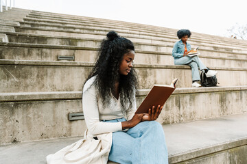 A female student reads a book while sitting on the bleachers