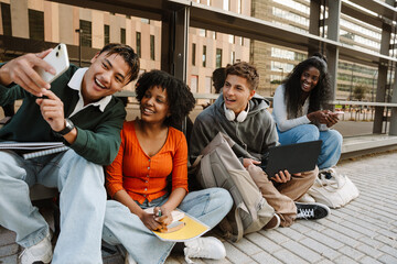 A group of four students sit and laugh while looking at a phone held by one of them