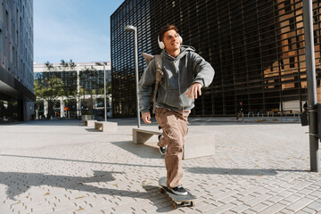 Male student rides a skateboard and smiles while listening in headphones © Drobot Dean