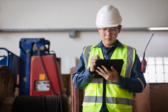 Engineer in PPE inspecting electrical power cable from a large cable reel, using a tablet for digital reporting. Industrial safety and energy infrastructure maintenance - Powered by Adobe