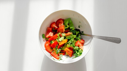Fresh vegetable salad with tomatoes, cucumbers, lettuce, and herbs in a white bowl on a bright table, symbolizing healthy eating, freshness, and natural vegetarian food