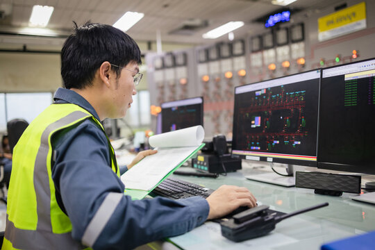 Engineer monitoring SCADA system in control room and documents, analyzing power grid operations on dual screens, energy management, automation, smart grid, and system supervision Concept