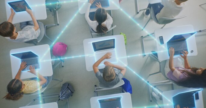 Children Interacting With Laptops, Tablets in Modern Classroom, Surrounded by Glowing Digital Connections. Concept Technology Integration and Prevalence of Artificial Intelligence. Rotating Top View.